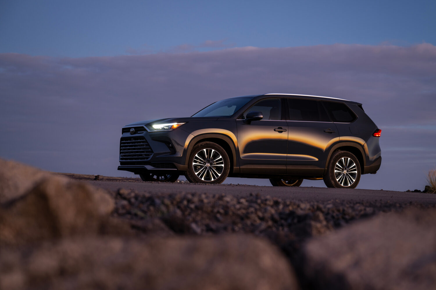 A 2026 Toyota GrandHighlander in a desert with it's lights on at dusk