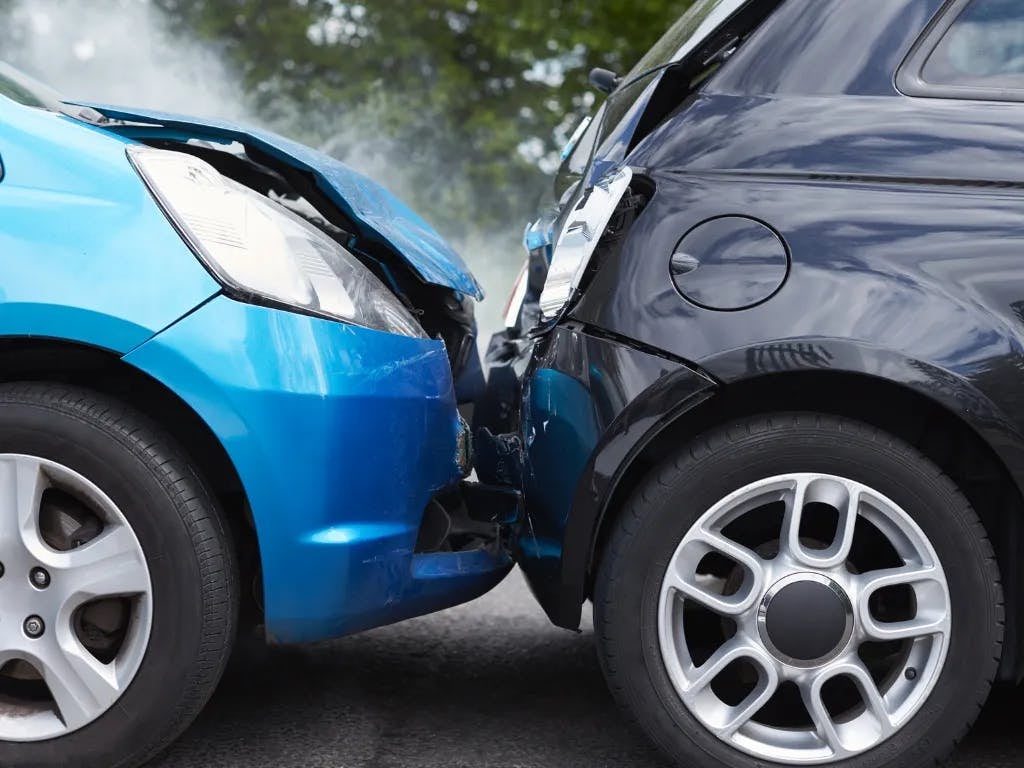 Two cars, one blue and one black, after a front-end collision with smoke emanating from the blue car.