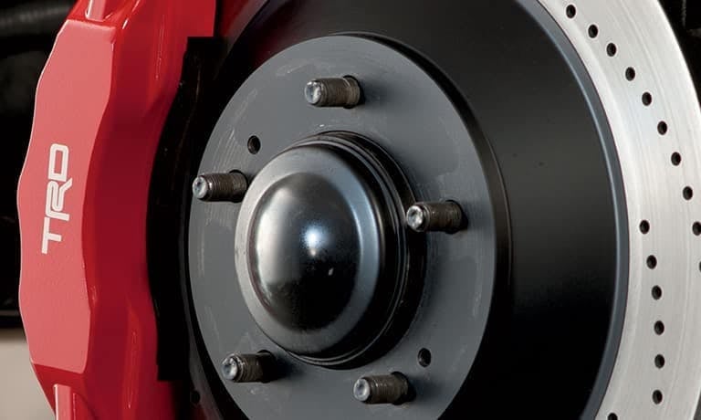 Red TRD branded brake caliper gripping a black and silver perforated brake rotor with wheel studs.