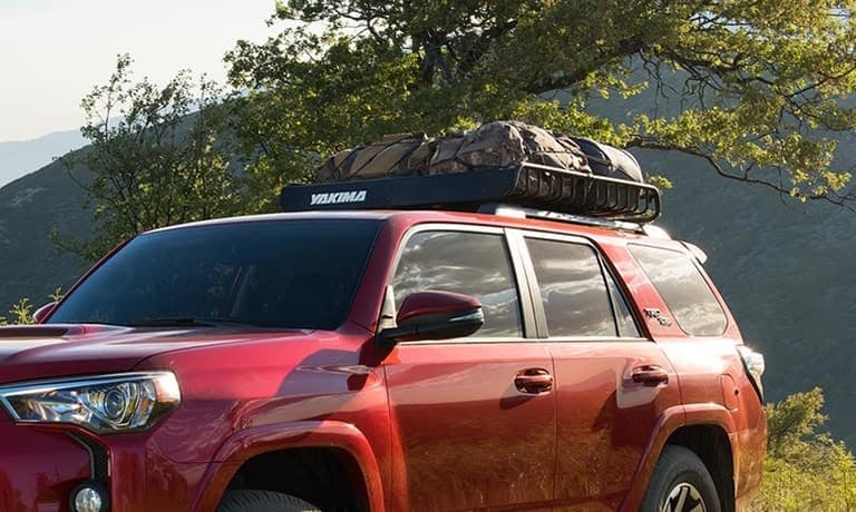 Red SUV with a Yakima roof rack carrying camping gear, parked in a lush, green mountainous landscape.