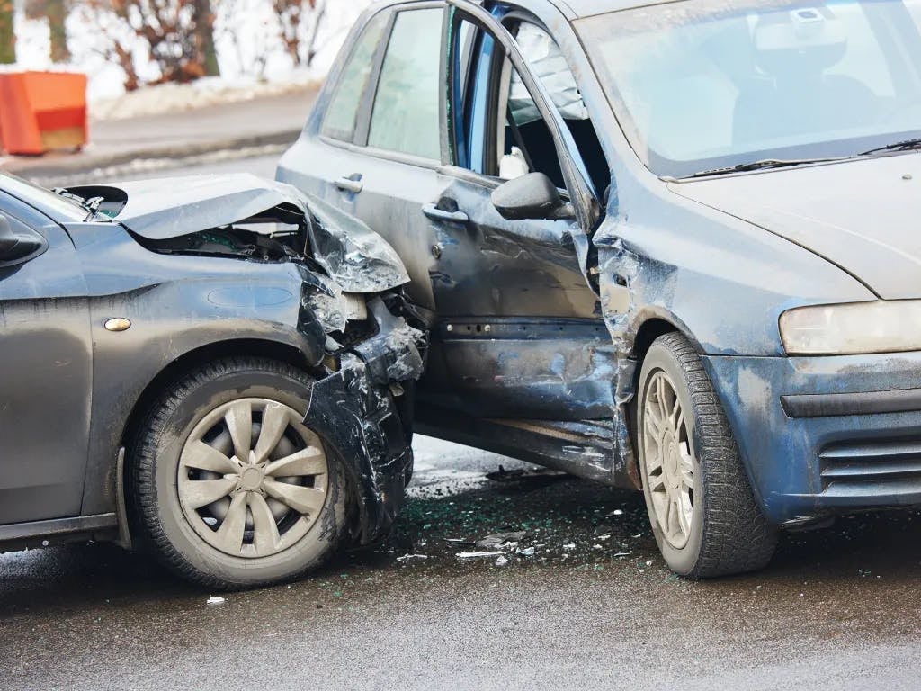 Two cars, one blue and one black, severely damaged and crumpled together at a T-bone intersection accident.